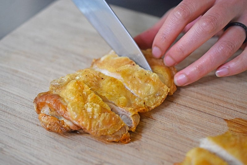 Slicing Air Fryer Cracklin' Chicken on a wooden cutting board.