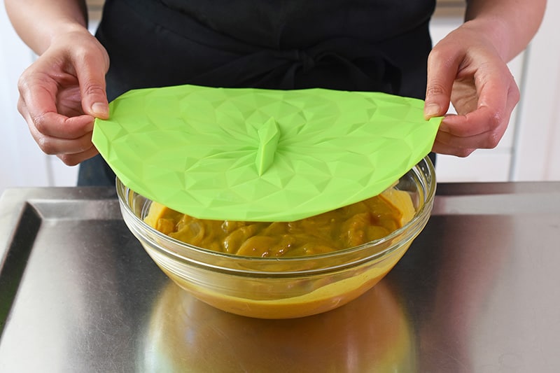Covering the bowl of marinated chicken with a green silicone lid.