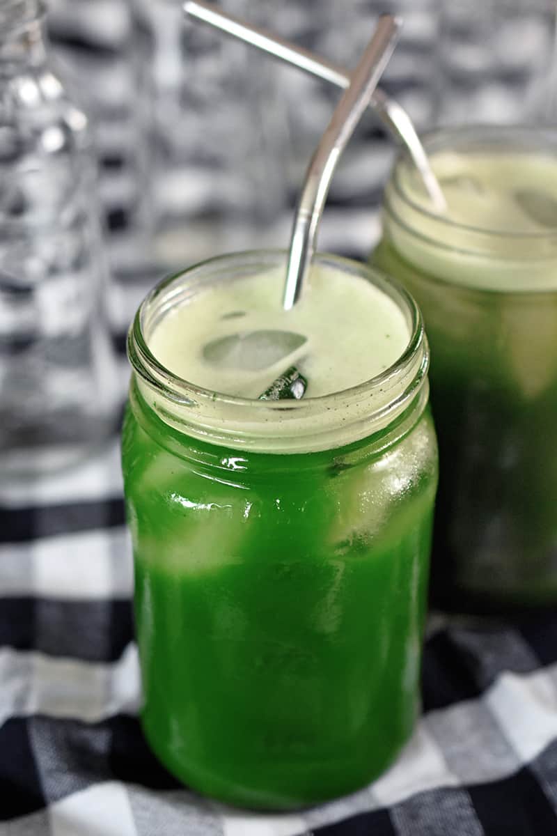 A shot of two mason jars filled with icy cold brew matcha with metal drinking straws inside.