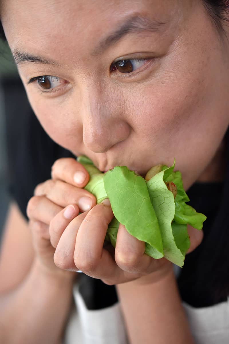 An Asian woman is biting into a lettuce wrap filled with Whole30 galbi, kimchi, and cauliflower rice. It's Paleo Korean food!