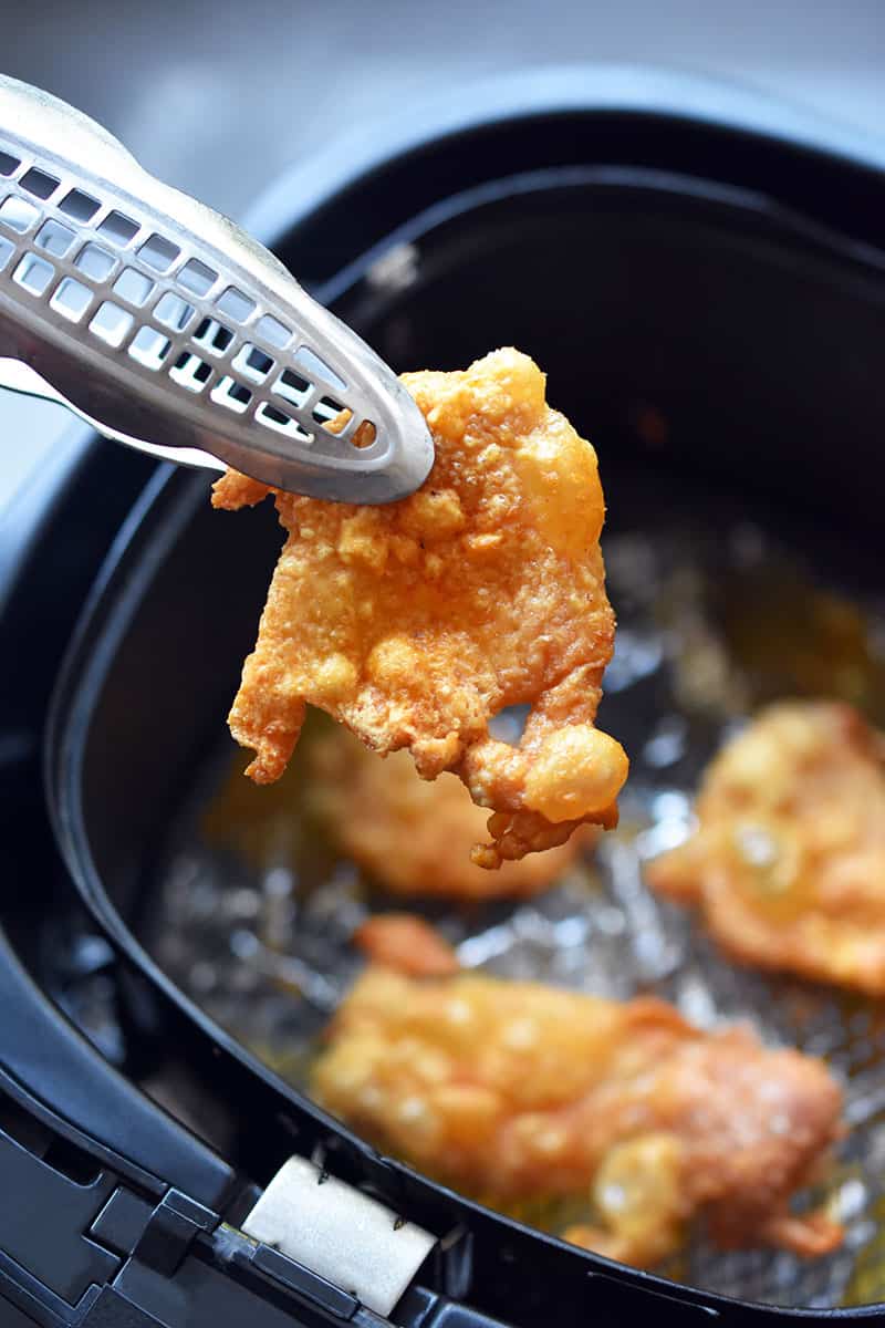 A pair of tongs are removing crispy chicken skins from an air fryer.