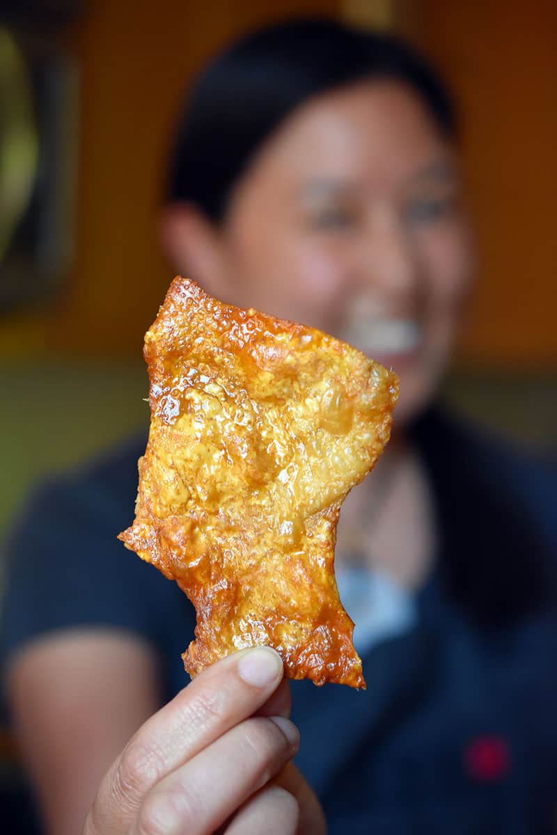A woman holding a piece of crispy chicken skins cooked in an air fryer.