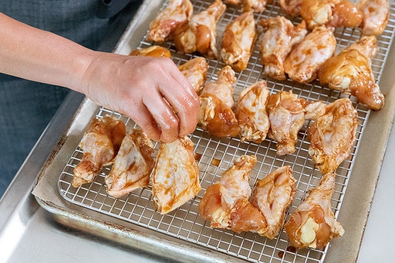 Placing Whole30 Chinese Chicken wings on a wire rack in a lined rimmed baking sheet.