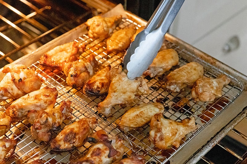 Flipping paleo Whole30 and gluten-free Chinese Chicken wings on a rack to cook them evenly in the oven.