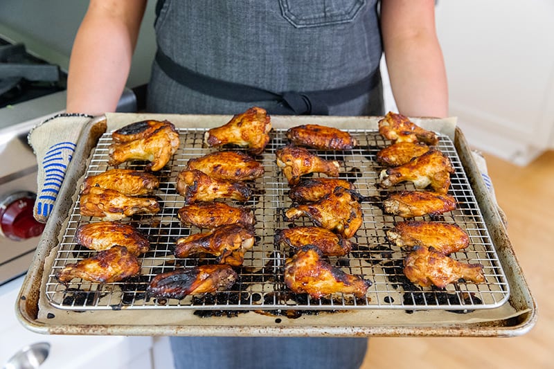 A person is holding a tray of gluten-free sticky Chinese Chicken Wings fresh out of the oven. 