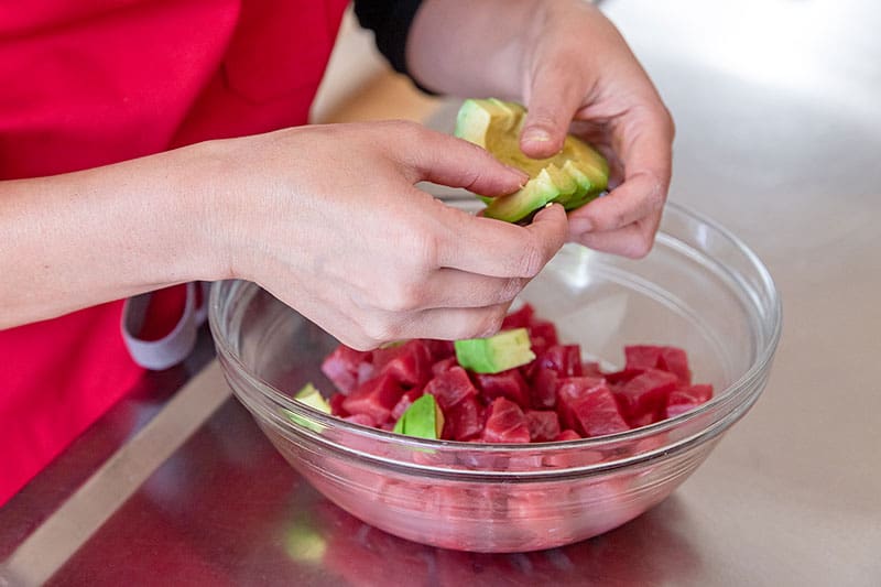 Adding avocado to a large bowl filled with raw diced tuna for a healthy paleo poke bowl.