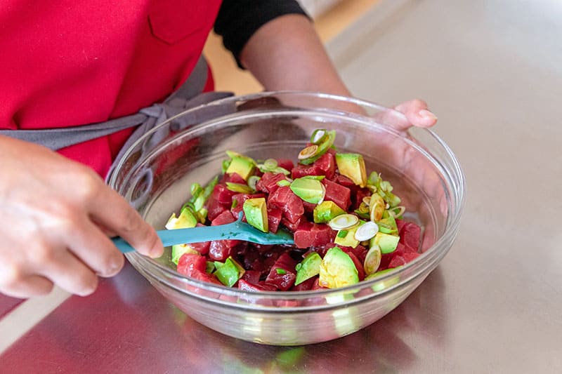 A person is carefully mixing the tuna poke with avocado in a bowl to mix the sauce well.