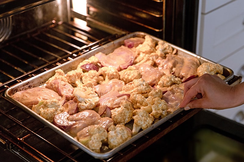 Placing a sheet pan tandoori chicken dinner into the oven.