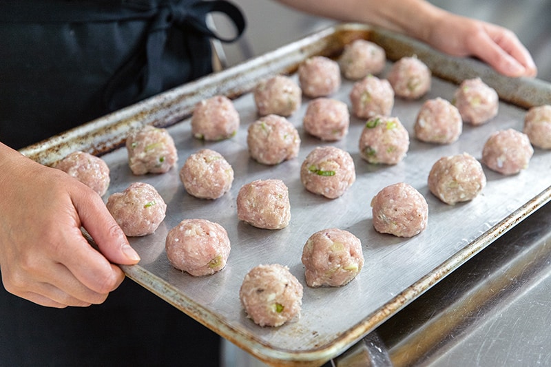 A rimmed baking sheet filled with Whole30 tsukune that is ready to be baked in the oven.
