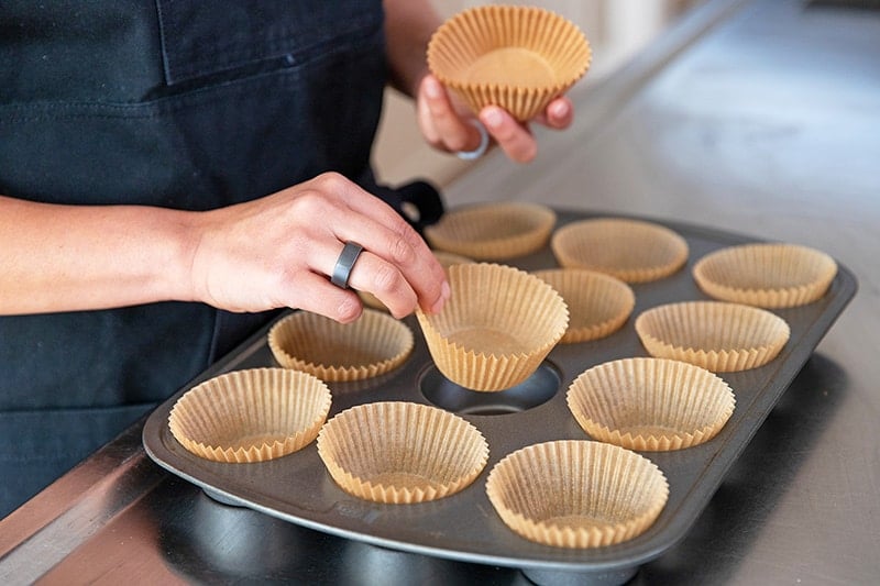 A person is adding parchment muffin liners to a muffin tin.