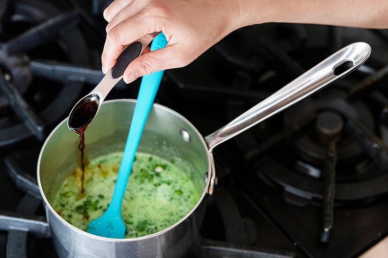 Pouring in vanilla extract into the small saucepan filled with hot coconut matcha milk.