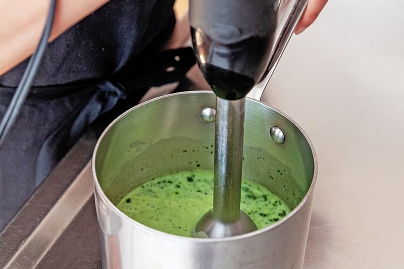 Blending the matcha coconut milk mixture with an immersion blender in the small saucepan.