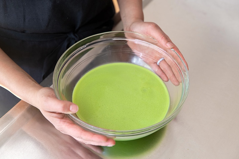 A medium bowl filled with matcha pudding ready for the refrigerator.