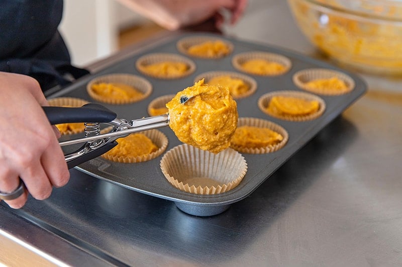 Someone using a disher to scoop the paleo almond flour muffins into the lined muffin tin.