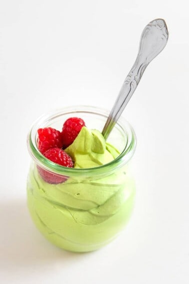 A side shot of matcha pudding in a clear glass with a serving spoon inside.
