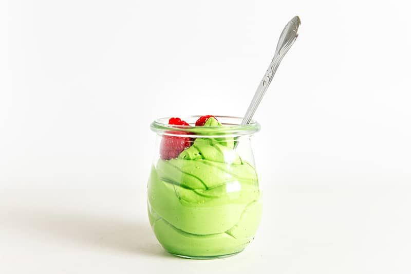 A side shot of dairy-free matcha pudding in a clear glass with a spoon inside.