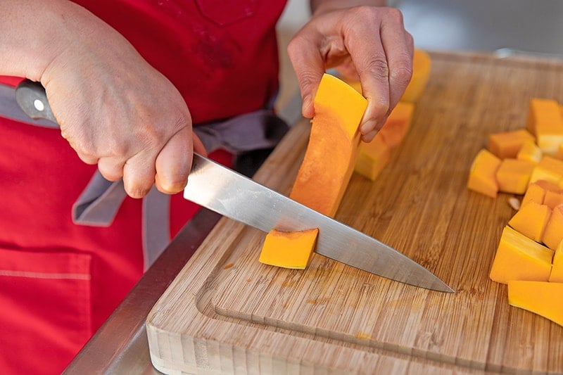A person in a red apron is cutting a butternut squash into cubes.