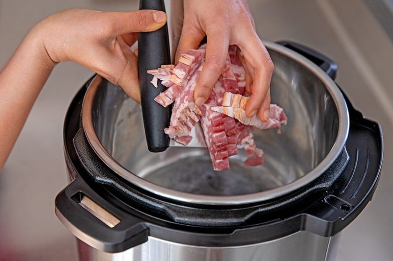 Adding thinly sliced bacon to an Instant Pot set on the saut function.