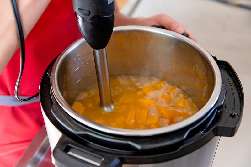 An overhead shot of an immersion blender in a pot of Instant Pot butternut squash soup.