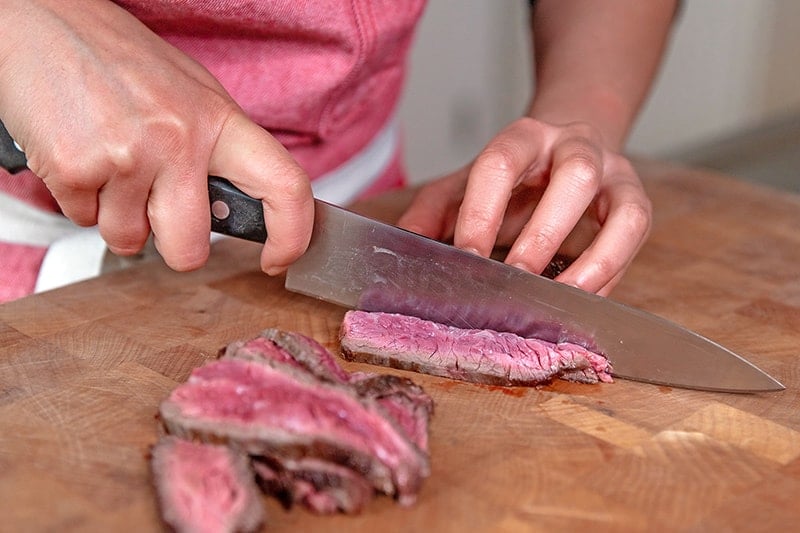 Cutting seared flank steak against the grain into thin strips for Whole30 Asian Steak Salad.