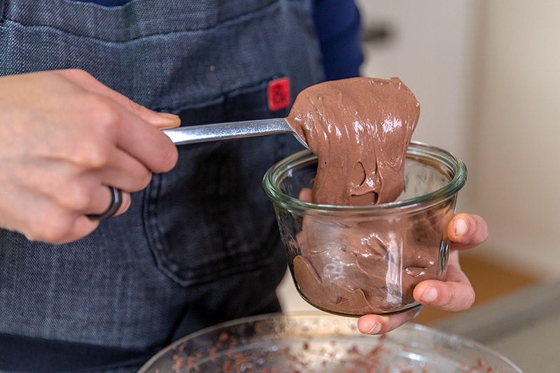 Someone spooning dairy-free paleo chocolate pudding into a glass container.