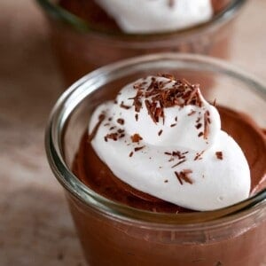 Two clear bowls filled with paleo chocolate pudding made with coconut milk and gelatin. The dairy-free chocolate pudding is topped with a dollop of whipped coconut cream and shaved dark chocolate.