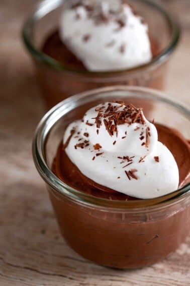Two clear bowls filled with paleo chocolate pudding made with coconut milk and gelatin. The dairy-free chocolate pudding is topped with a dollop of whipped coconut cream and shaved dark chocolate.