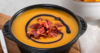 A black bowl filled with Instant Pot Butternut Squash Soup on a wooden cutting board.