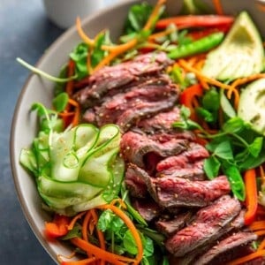 An overhead shot of Whole30 and Paleo Asian Steak Salad, a large white bowl topped with colorful vegetables and sliced seared flank steak.