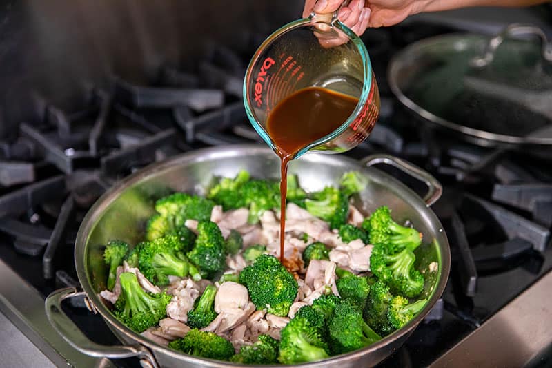 Pouring All-Purpose Stir-Fry Sauce into a pan of Whole30 chicken and broccoli stir-fry.