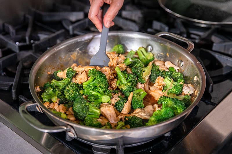 An overhead shot of paleo chicken and broccoli stir fry cooking in a large skillet.