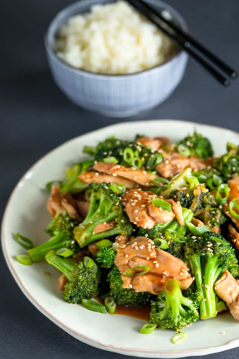 A large white platter topped with Whole30, paleo, and gluten-free chicken and broccoli stir fry in front of a blue bowl of cauliflower rice.