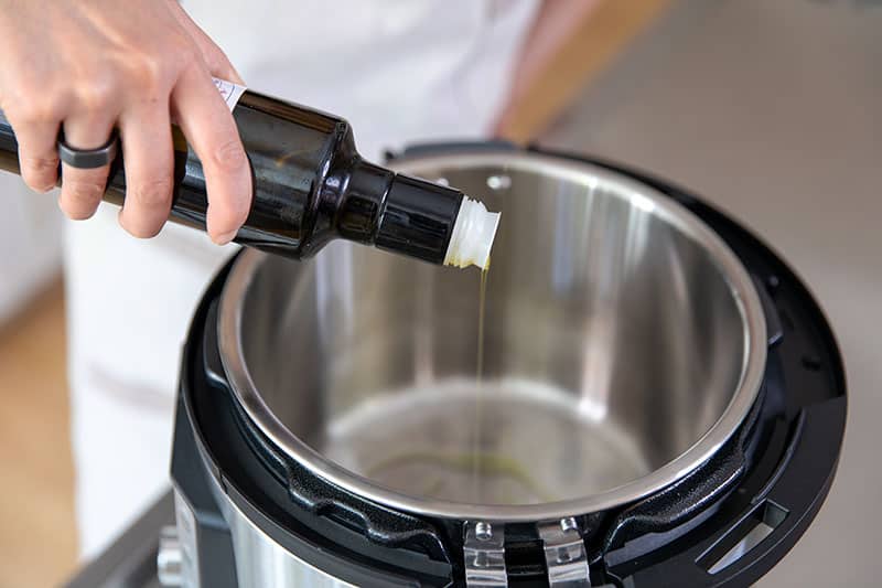 An overhead shot of someone pouring extra virgin olive oil into an open Instant Pot on the sauté function.