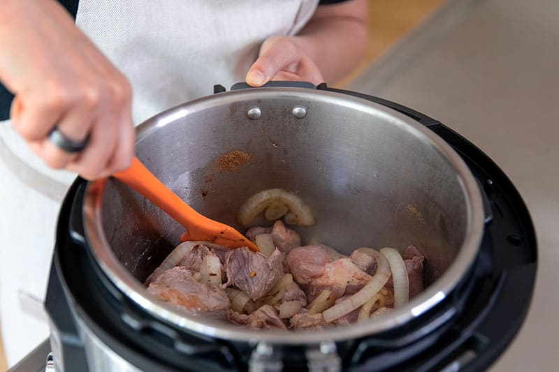 Stirring the contents of an Instant Pot filled with ingredients to make paleo and Whole30 pork and cabbage stew.
