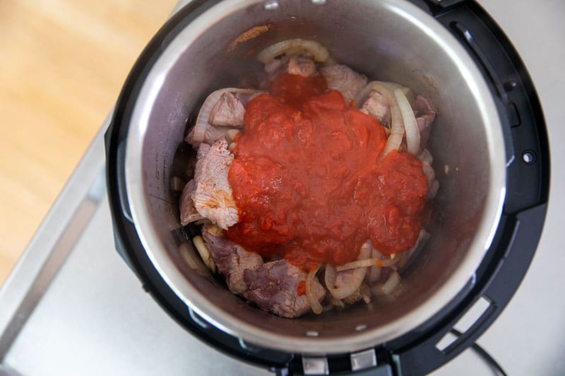 An overhead shot of an open Instant Pot with pork stew covered topped with marinara sauce.