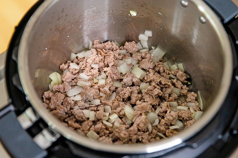 An overhead shot of an open Instant Pot with cooked bulk Italian sausage and onions inside.