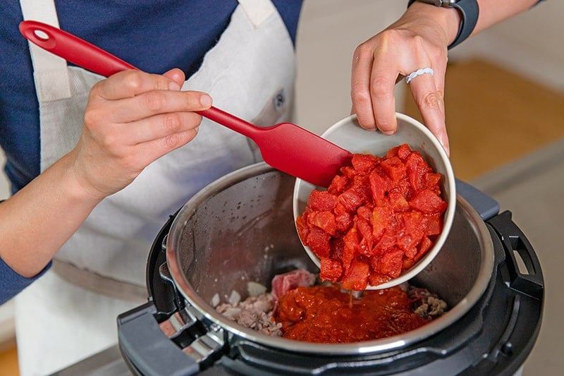 Adding drained diced tomatoes to the Instant Pot to make an easy meat sauce.