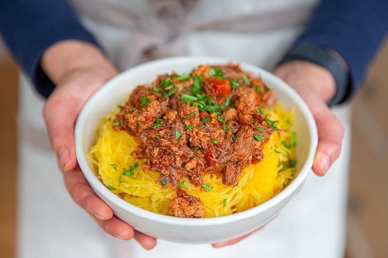 An overhead shot of two hands holding a bowl of spaghetti squash covered with Instant Pot meat sauce.