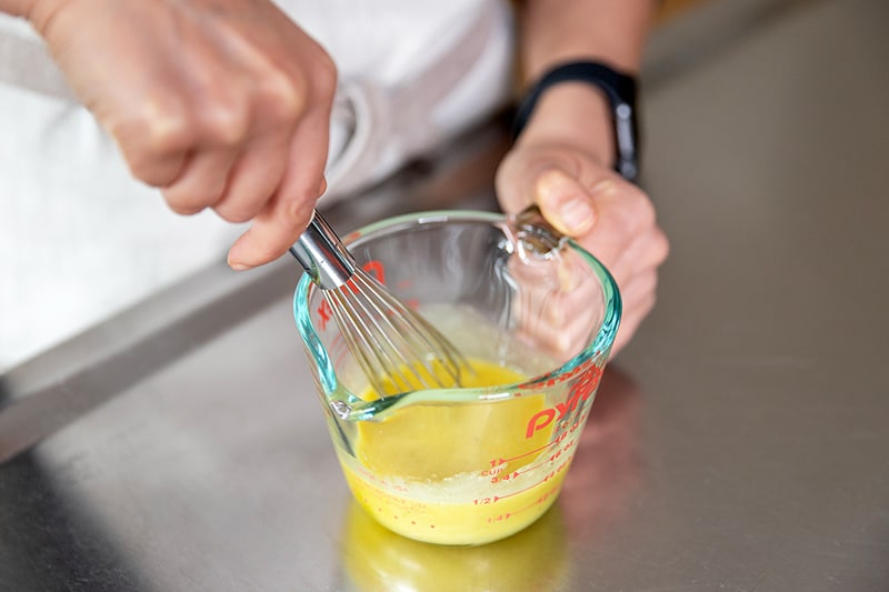 Whisking the lemon vinaigrette in a small liquid measuring cup for kale salad.