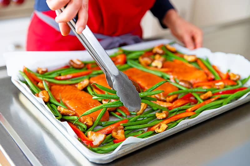 Arranging the vegetables in a single layer around the teriyaki salmon on the sheet pan.