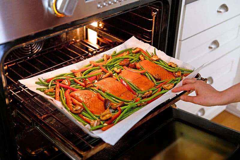 Placing paleo-friendly sheet pan teriyaki salmon into the oven to cook.