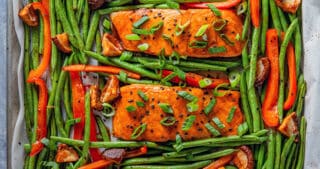 An overhead shot of Whole30 and paleo Teriyaki Salmon Sheet Pan, four cooked salmon fillets surrounded with cooked green beans and bell peppers.