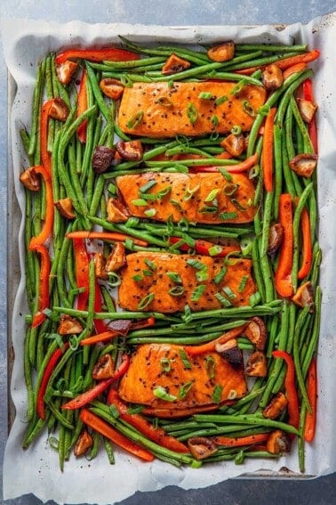 An overhead shot of Whole30 and paleo Teriyaki Salmon Sheet Pan, four cooked salmon fillets surrounded with cooked green beans and bell peppers.