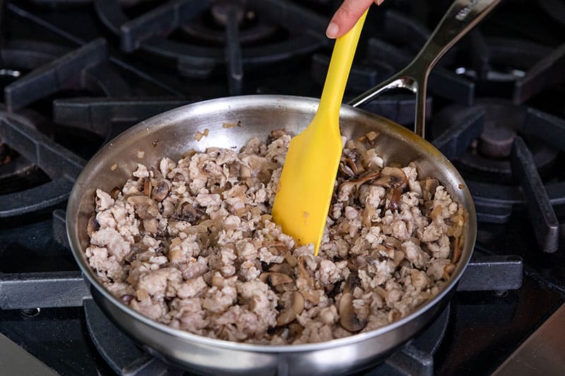 A stainless steel skillet is filled with cooked Italian sausage, onions, and mushrooms.