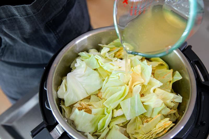 Pouring broth into an Instant Pot filled with the ingredients for Ethiopian cabbage stew.