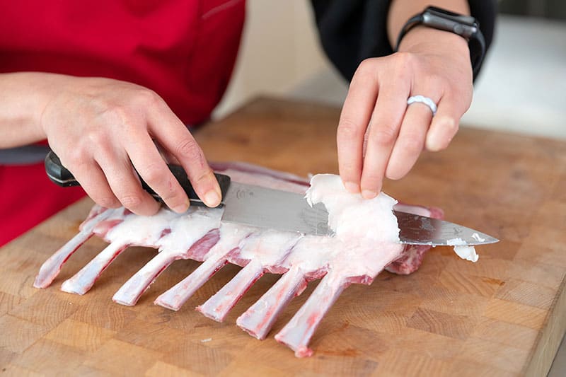 Trimming extra fat off of the top of a rack of lamb with a chef's knife.