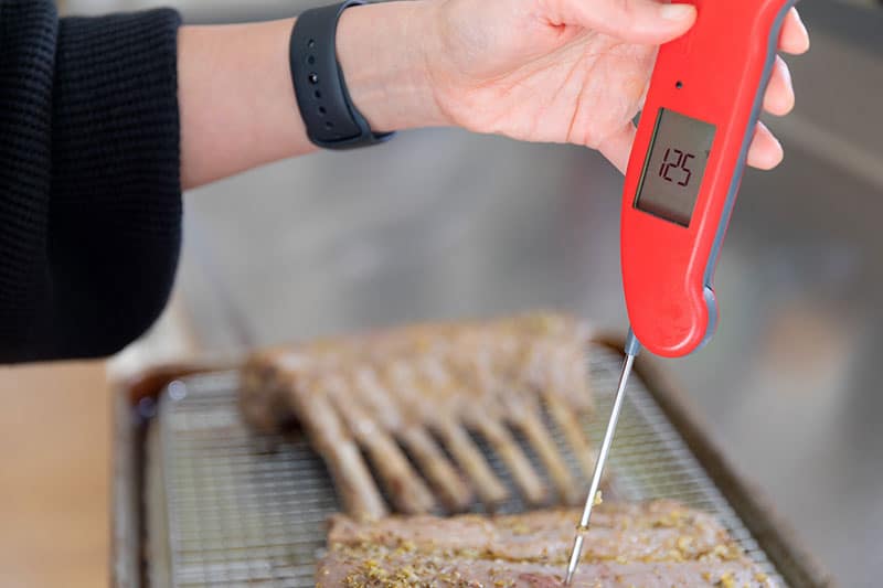 A red instant-read thermometer stuck in a rack of lamb reads "125"
