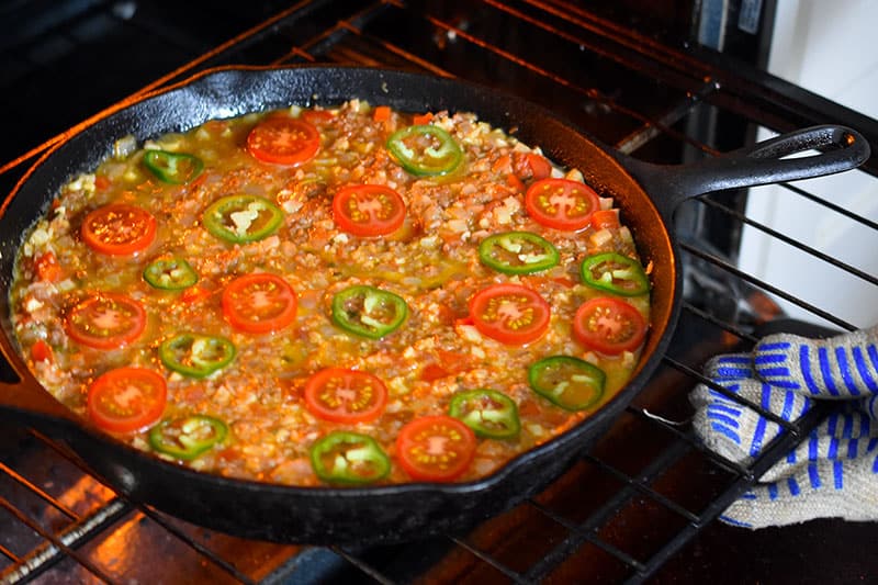 Someone putting a cast iron skillet filled with Nom Nom Paleo's Tex-Mex Beef and Rice Casserole, a grain-free one pan dinner.