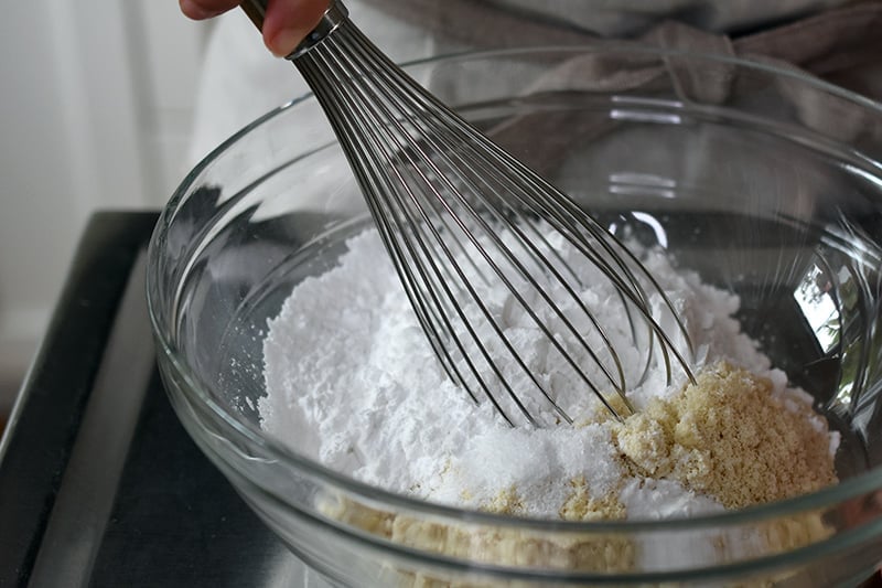 Whisking the dry ingredients for paleo cinnamon rolls in a large glass bowl.