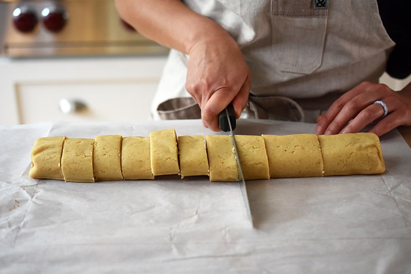Someone slicing the rolled dough into twelve even pieces with a sharp knife.